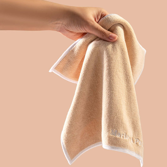 Hand holding a beige towel with white trim against a beige background