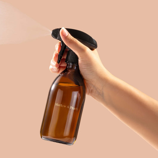 Hand holding a brown spray bottle with a black nozzle against a beige background